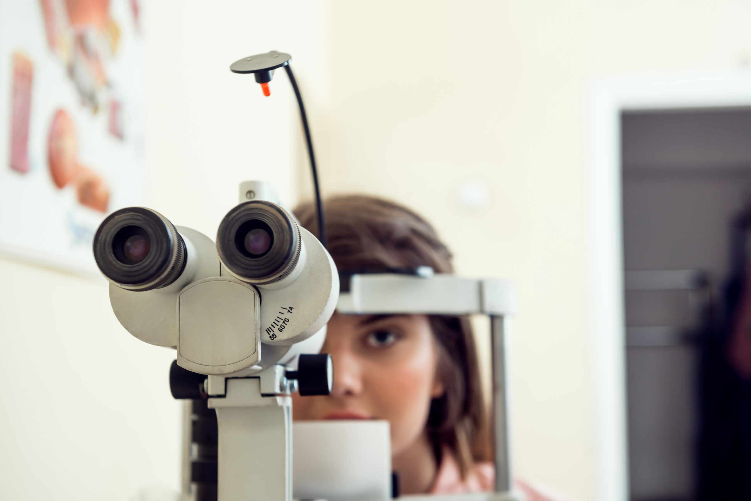 Portrait of cute caucasian female patient sitting in optometrist office, waiting for start of procedure to check her vision with microbioscope, sitting over yellow background. Ophthalmology concept.